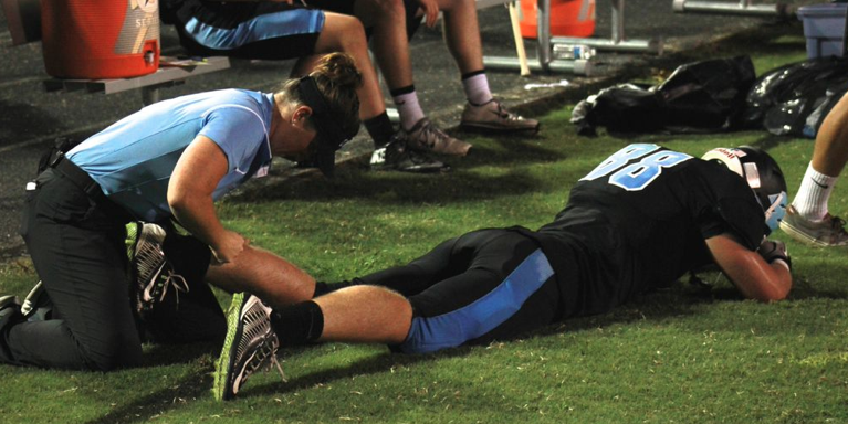 Trainer Katie Brodka tends to an injury on the sideline of a football game.  Photo by Nick Anderson.