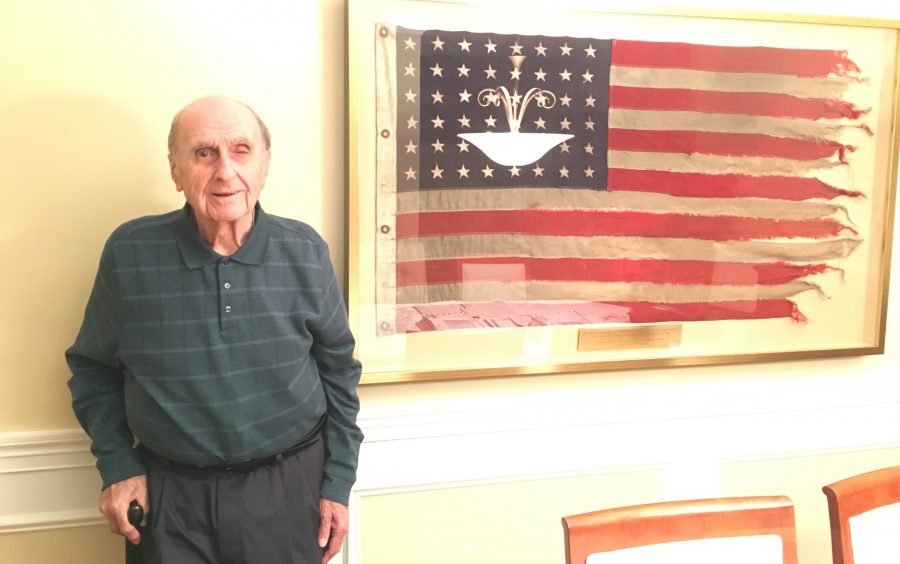 Former US Quartermaster Stephen Berberian stands beside the flag that flew on the ship he steered across the English Channel to Omaha beach on D-Day. Photo by Jennah Haque.