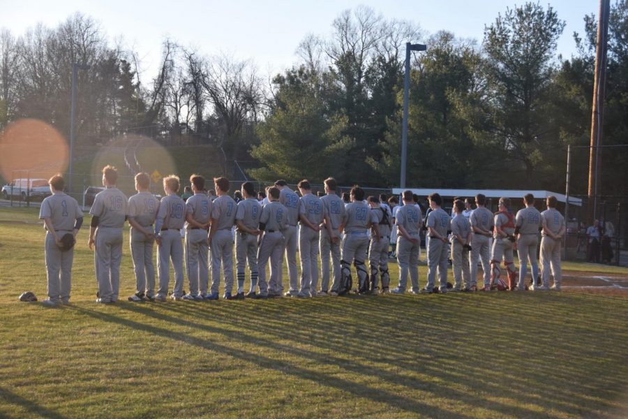 The baseball team looks out into right field while standing for the national anthem.