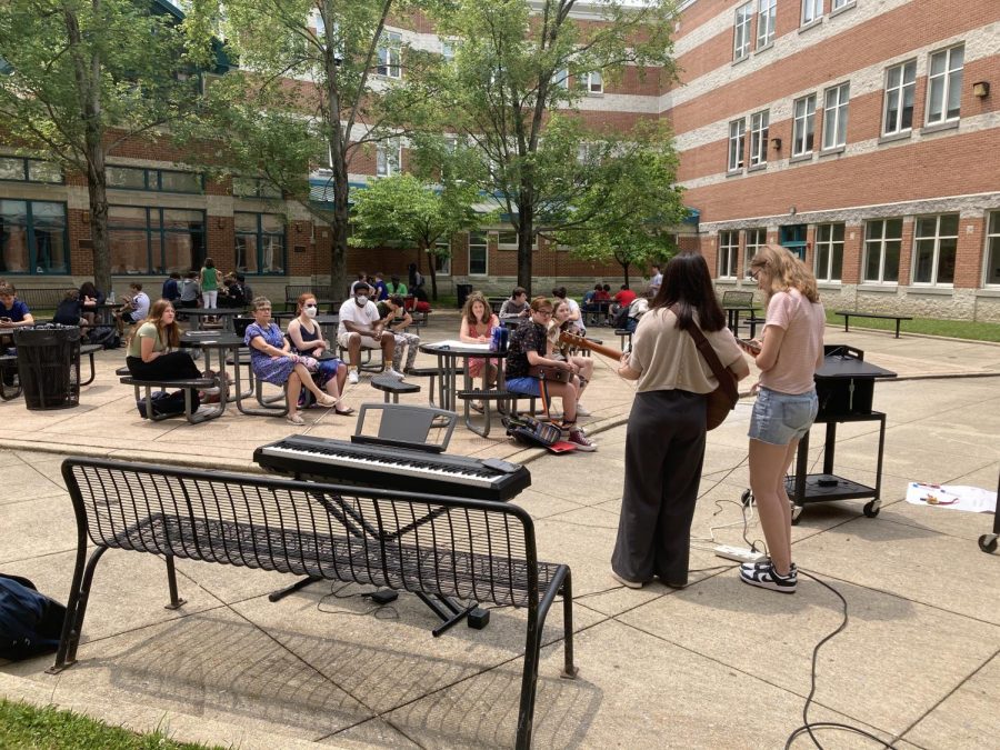 Students and teachers listen to a performance at an open mic event in the courtyard during lunch.