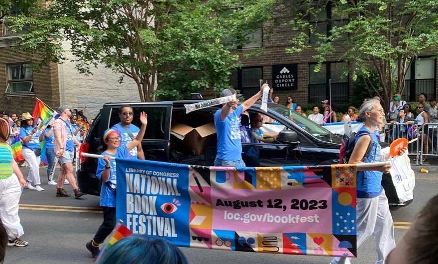 Attendees of the 2023 DC Capital Pride Parade carry a sign advertising the National Book Festival.