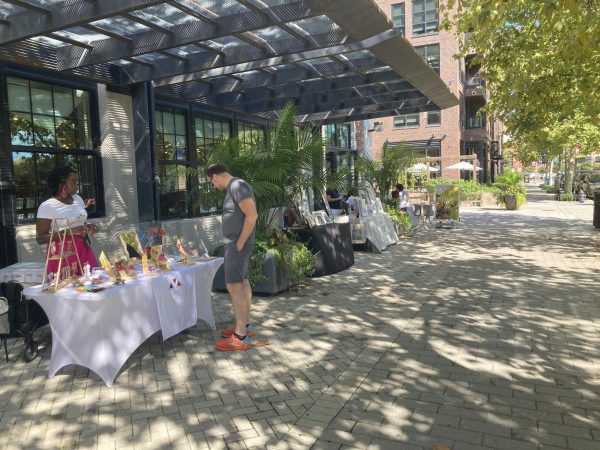 White-clothed tables line the Steadfast Supply store’s exterior, each covered with products ranging from colorful earrings to ornate canvas paintings.